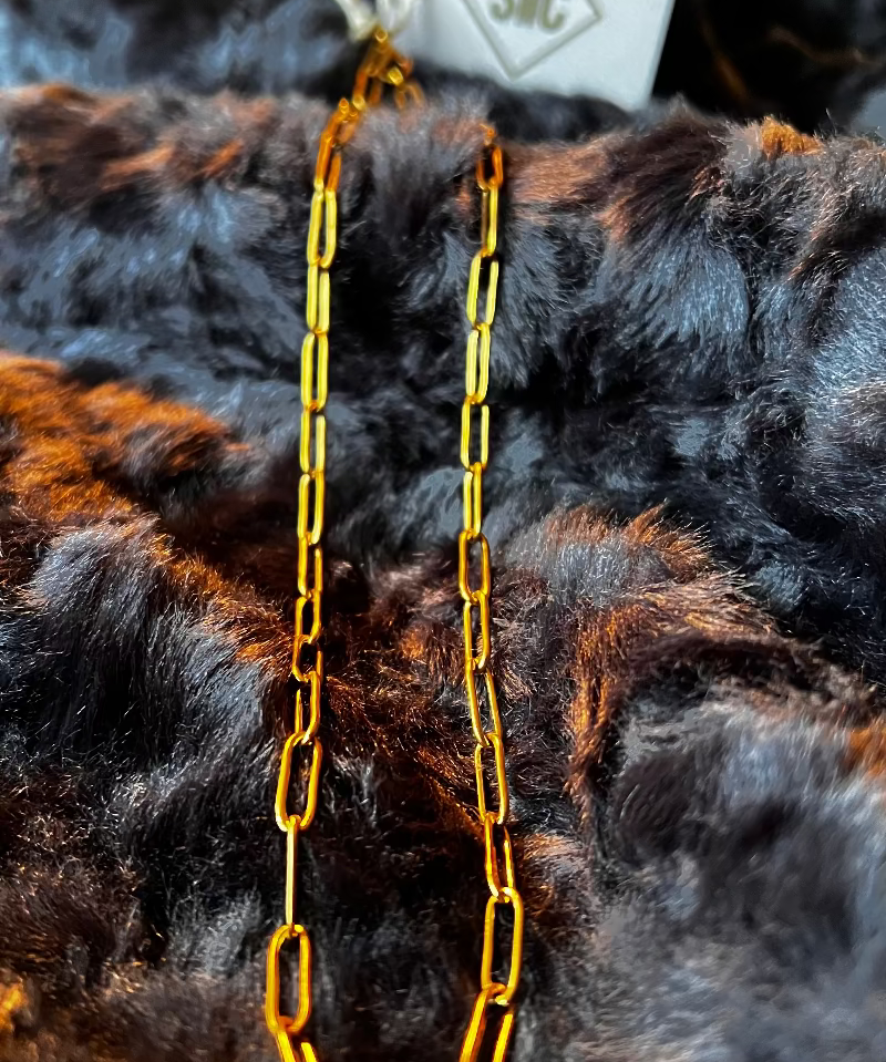 Gold chain necklace on a dark fur background with a visible brand tag.