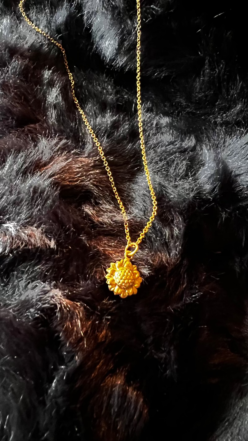 Gold necklace with a sunflower pendant on a black fur background