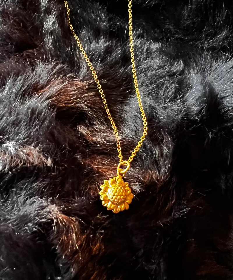 Gold necklace with a sunflower pendant on a black fur background