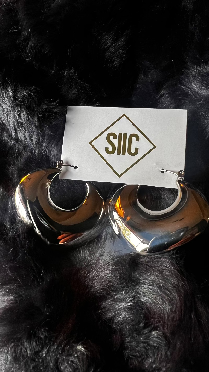 Silver hoop earrings on a black fur background with 'SIIC' card.