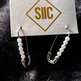 Pair of earrings on a card with 'SIIC' branding against a dark fur background