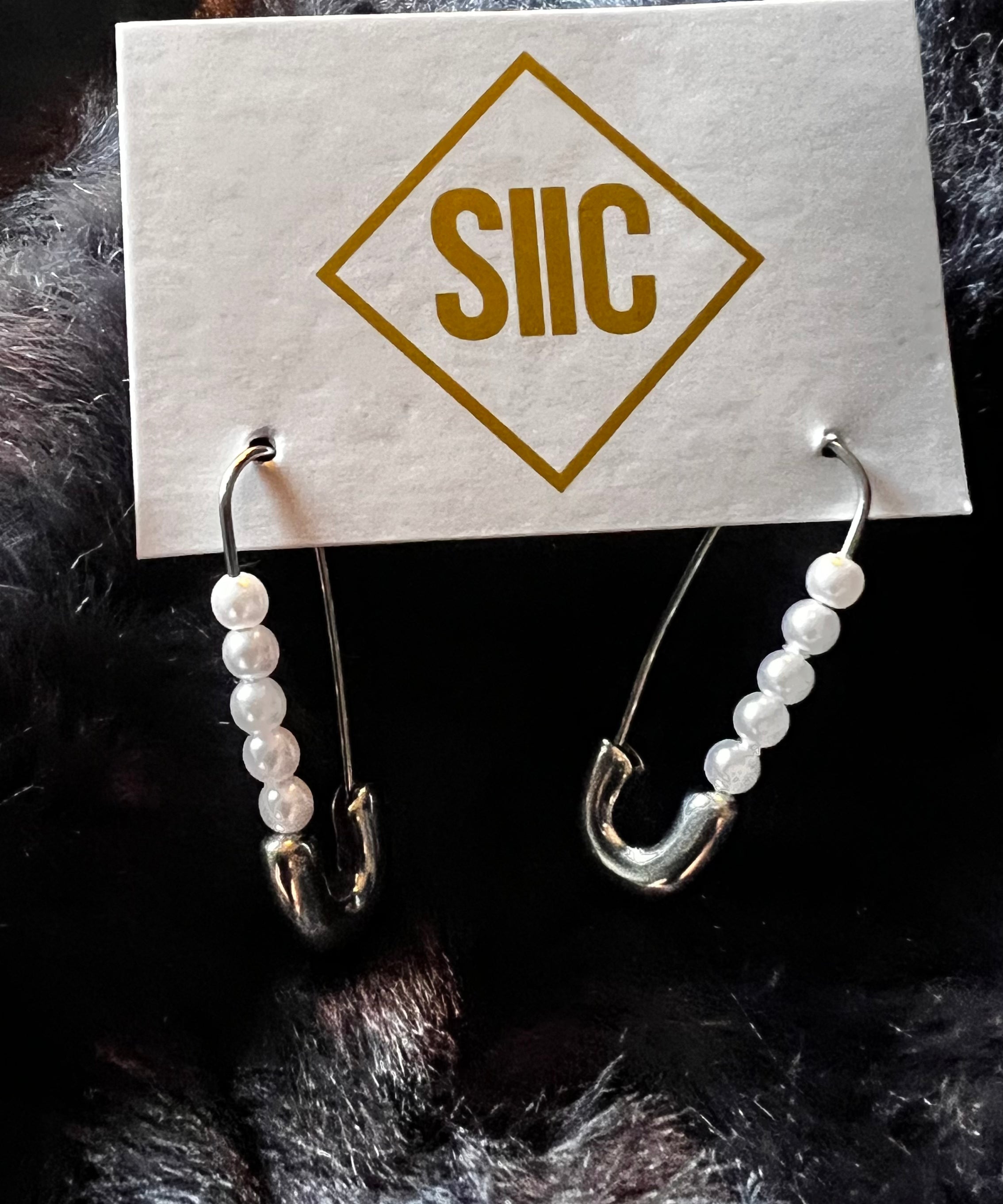 Pair of earrings on a card with 'SIIC' branding against a dark fur background