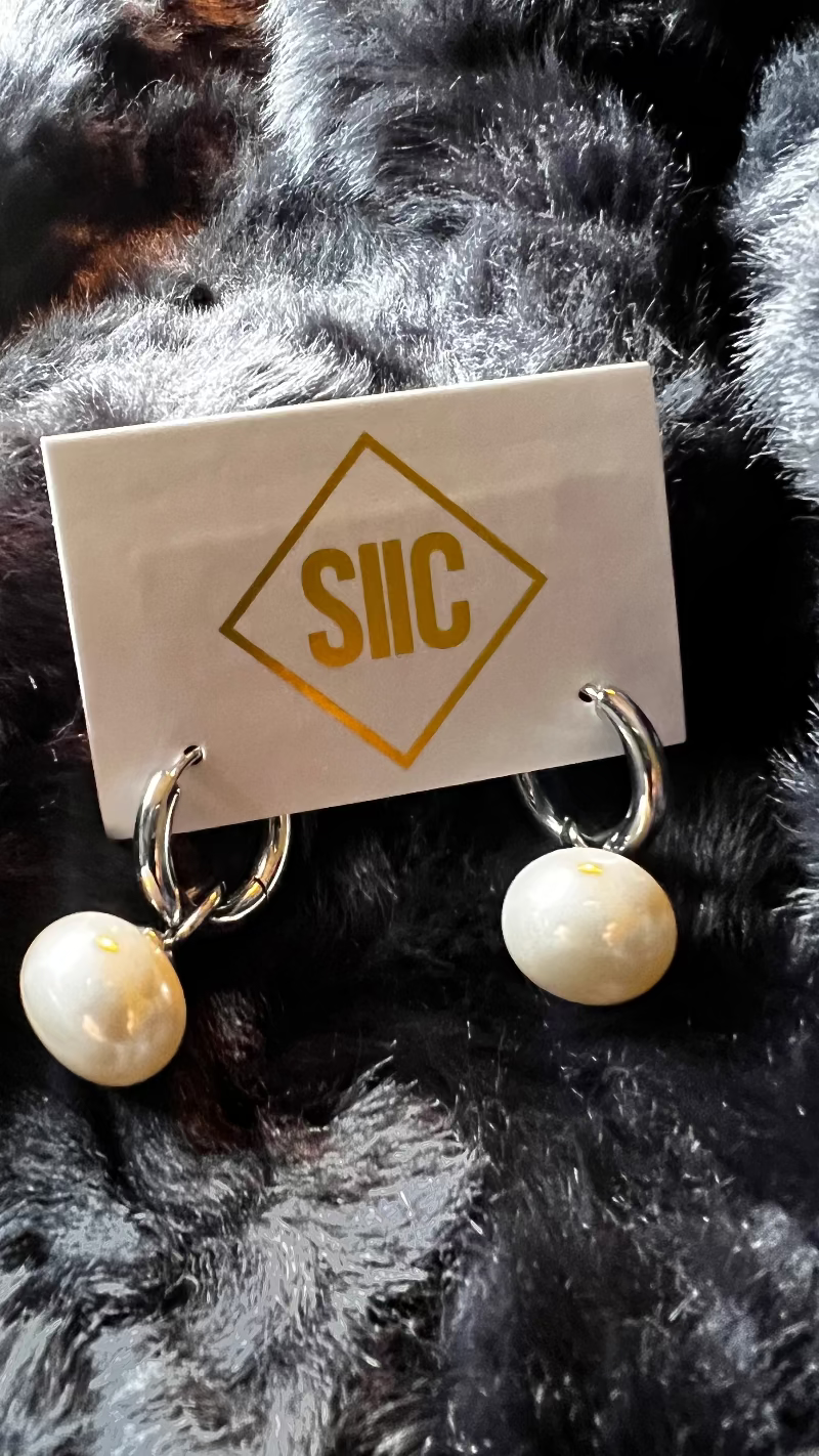 Pair of pearl earrings on a card with 'SIIC' branding against a fur background