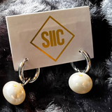 Pair of pearl earrings on a card with 'SIIC' branding against a fur background