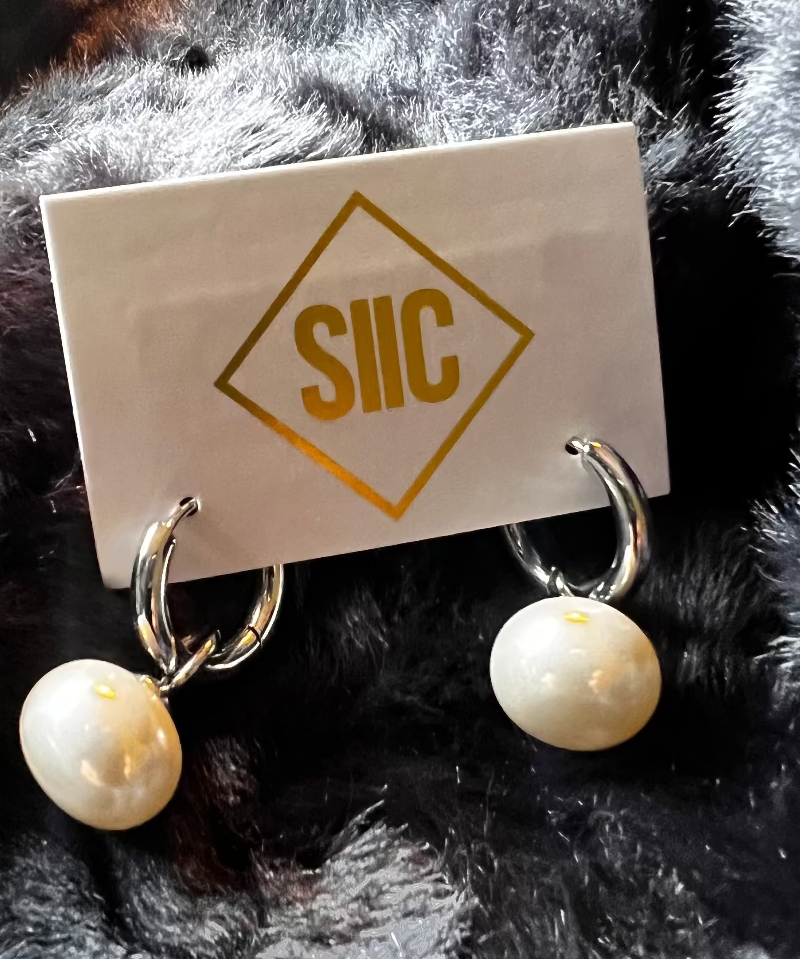 Pair of pearl earrings on a card with 'SIIC' branding against a fur background