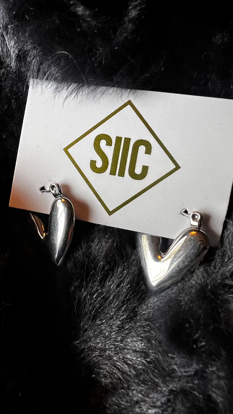 Silver earrings on a card with 'SIIC' logo against a dark fur background