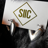 Silver earrings on a card with 'SIIC' logo against a dark fur background