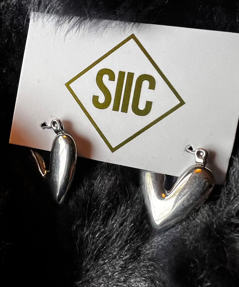 Silver earrings on a card with 'SIIC' logo against a dark fur background