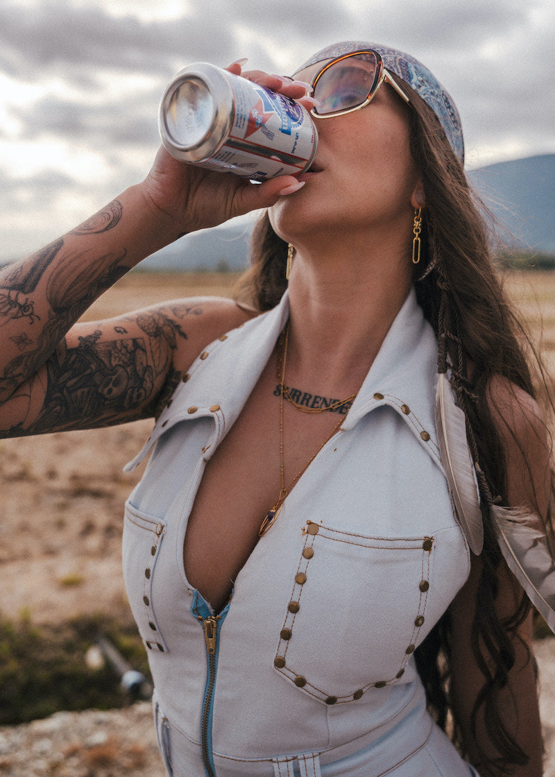 Woman drinking from a can outdoors with mountains in the background wearing soul sister since 1969