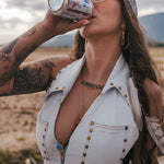 Woman drinking from a can outdoors with mountains in the background wearing soul sister since 1969