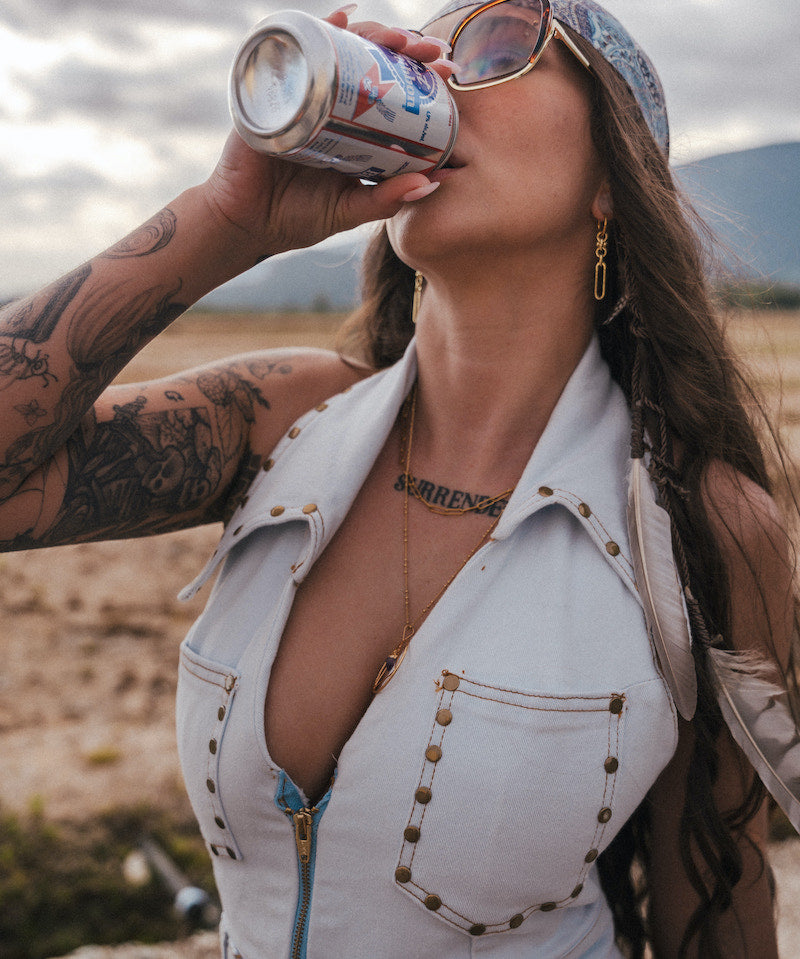 Woman drinking from a can outdoors with mountains in the background wearing soul sister since 1969