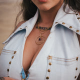 Close-up of a person wearing a light blue denim jacket with gold buttons, gold necklace, and sunglasses wearing soul sister since 1969.