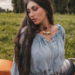 Woman in a light blue blouse by Soul Sister since 1969 sitting on a motorcycle in a grassy field with trees in the background