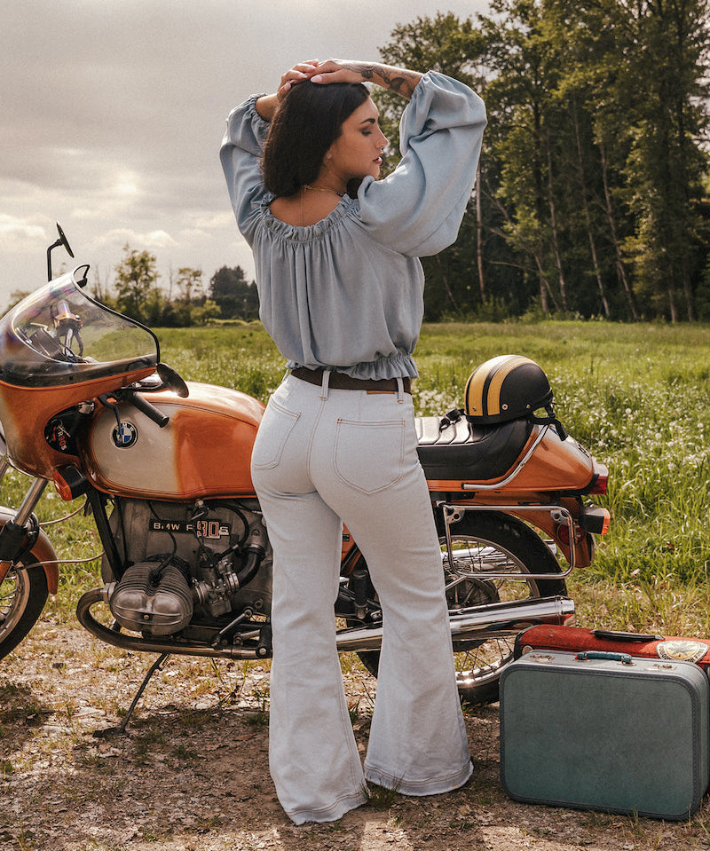 Woman standing next to a motorcycle in a field with a suitcase nearby wearing a sweet Jane peasant blouse by Soul Sister since 1969