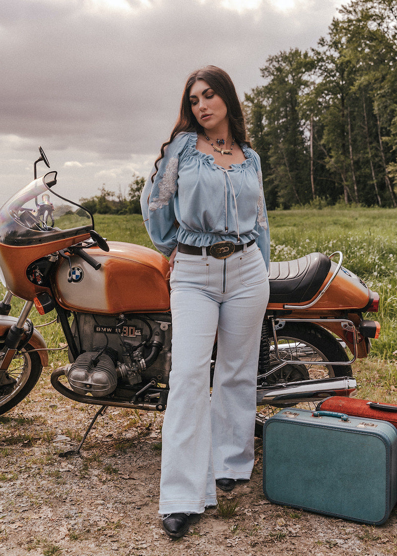 Woman standing next to a vintage motorcycle with a suitcase in a field wearing Soul Sister since 1969