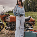 Woman standing next to a vintage motorcycle with a suitcase in a field wearing Soul Sister since 1969