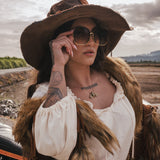 Woman in a white dress and brown hat with sunglasses, standing outdoors. wearing soul sister since 1969