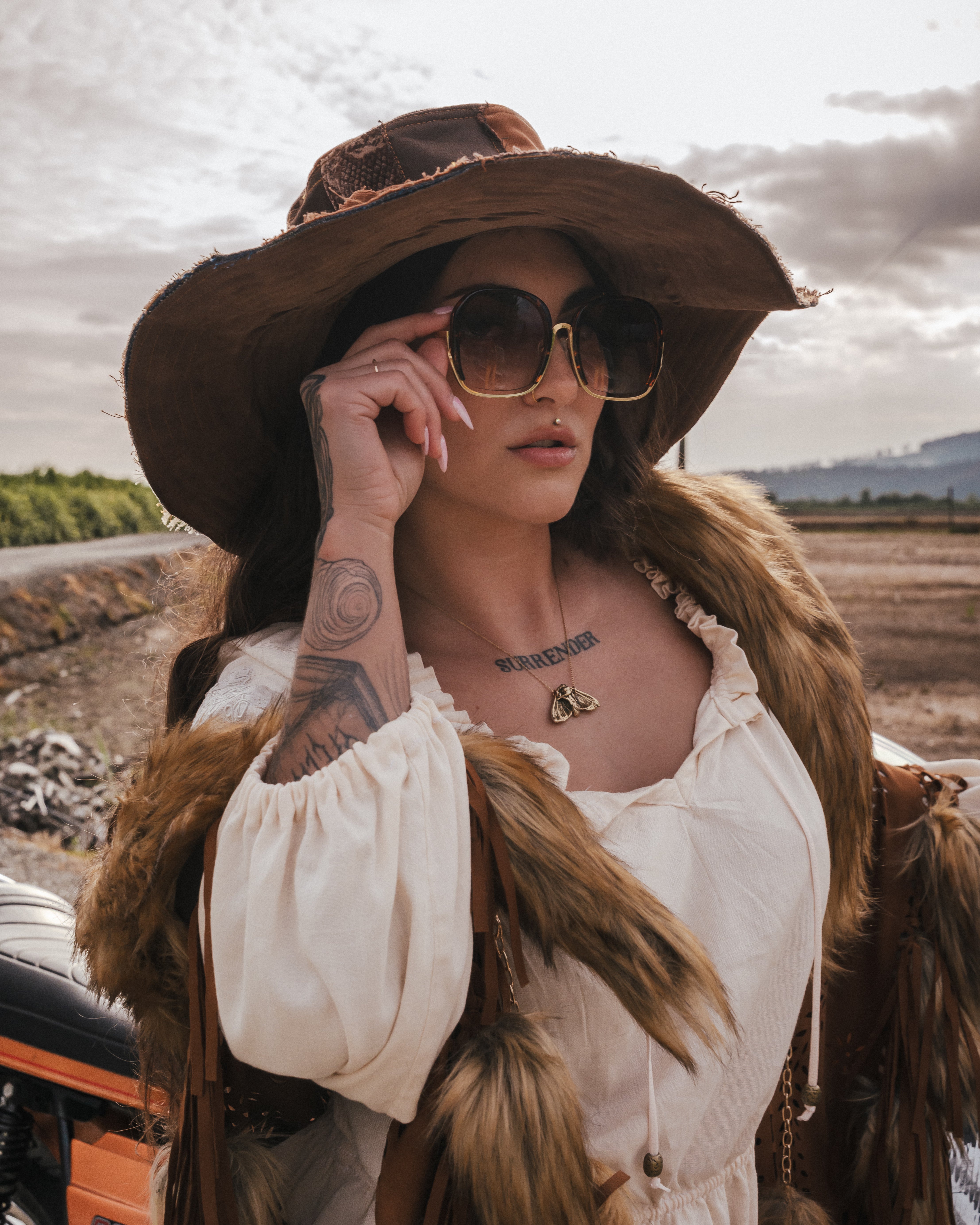 Woman in a white dress and brown hat with sunglasses, standing outdoors. wearing soul sister since 1969