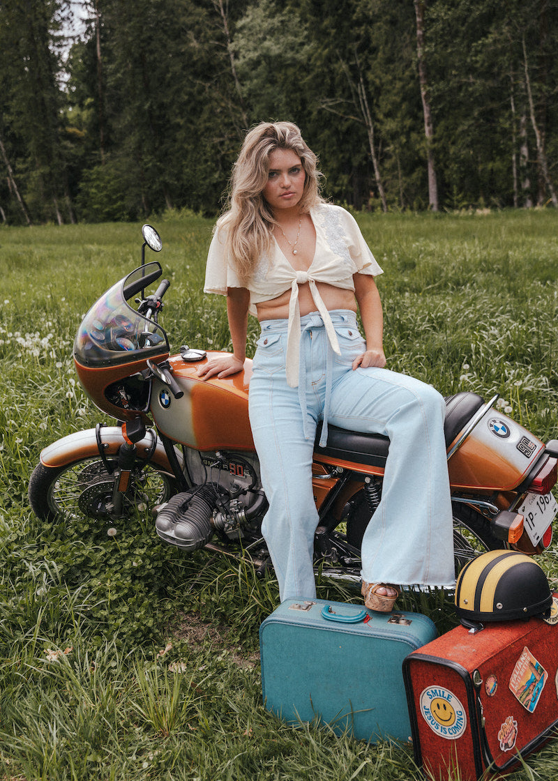 Woman sitting on a motorcycle with suitcases in a grassy field Soul Sister since 1969.