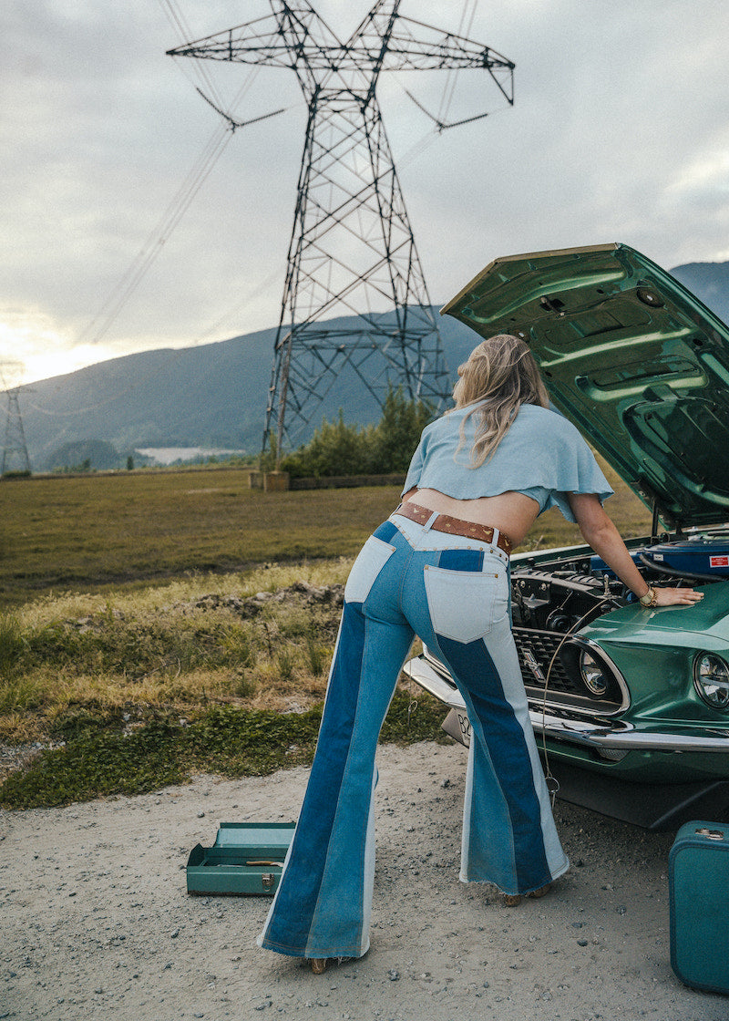 Person in blue and white outfit working on a green car in an open field with power lines in the background Wearing Soul Sister since 1969. .