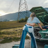 Person in blue and white outfit working on a green car in an open field with power lines in the background Wearing Soul Sister since 1969. .