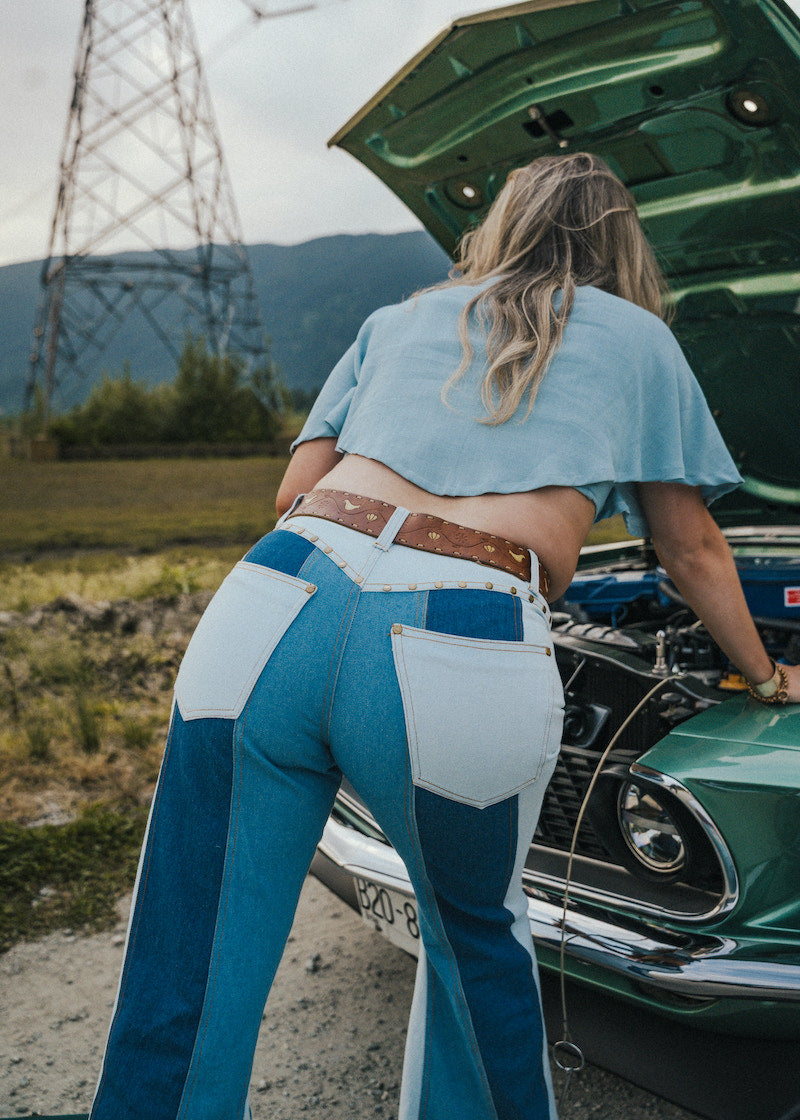 Person wearing blue jeans and a light blue top standing next to an open car hood outdoors Wearing Soul Sister since 1969. .