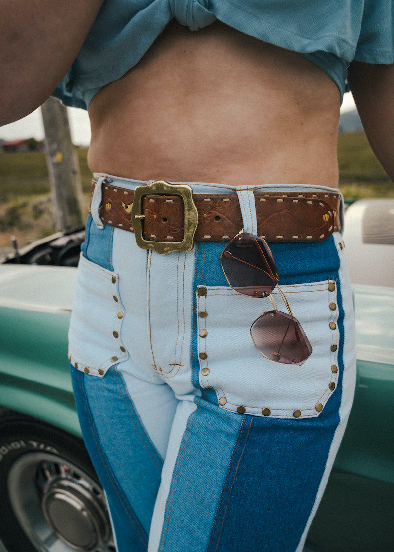 Person wearing a blue shirt and white pants with a brown belt and sunglasses, standing next to a vintage car Wearing Soul Sister since 1969. 