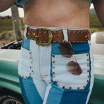 Person wearing a blue shirt and white pants with a brown belt and sunglasses, standing next to a vintage car Wearing Soul Sister since 1969. 