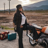 Woman sitting on a motorcycle with suitcases nearby, set against a scenic background wearing Soul Sister since 1969.