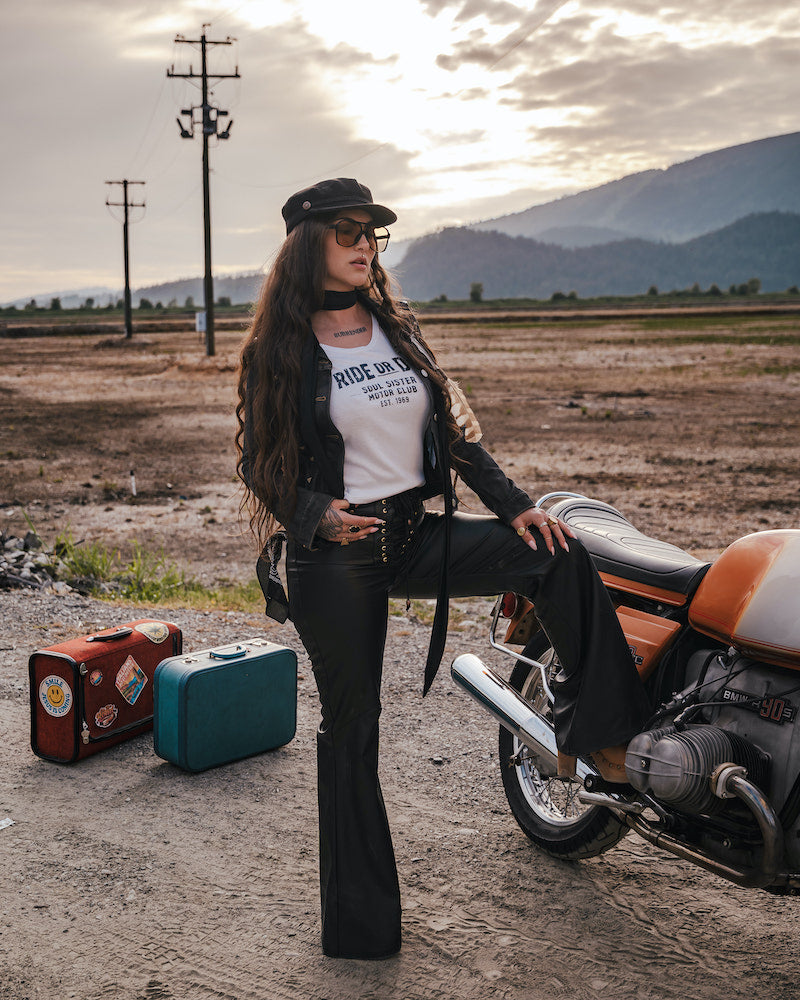 Woman in a desert setting with a motorcycle and suitcases, wearing a 'Ride or Die' t-shirt designed and made by Soul Sister since 1969.