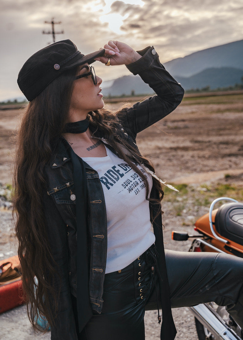 Woman with long hair and a hat standing outdoors with mountains in the background wearing Soul Sister since 1969.