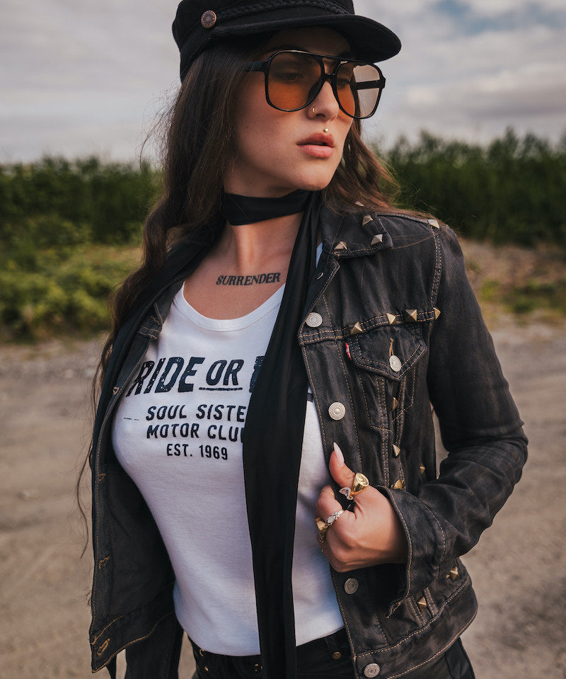 Woman wearing a black jacket, white t-shirt, and sunglasses outdoors wearing Soul Sister since 1969.