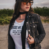 Woman wearing a black jacket, white t-shirt, and sunglasses  and a black hat outdoors wearing Soul Sister since 1969.