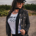 Woman wearing a black jacket, white t-shirt with text, and sunglasses outdoors wearing Soul Sister since 1969.