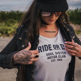 Person wearing a white t-shirt with text, black jacket, and cap outdoors wearing Soul Sister since 1969.