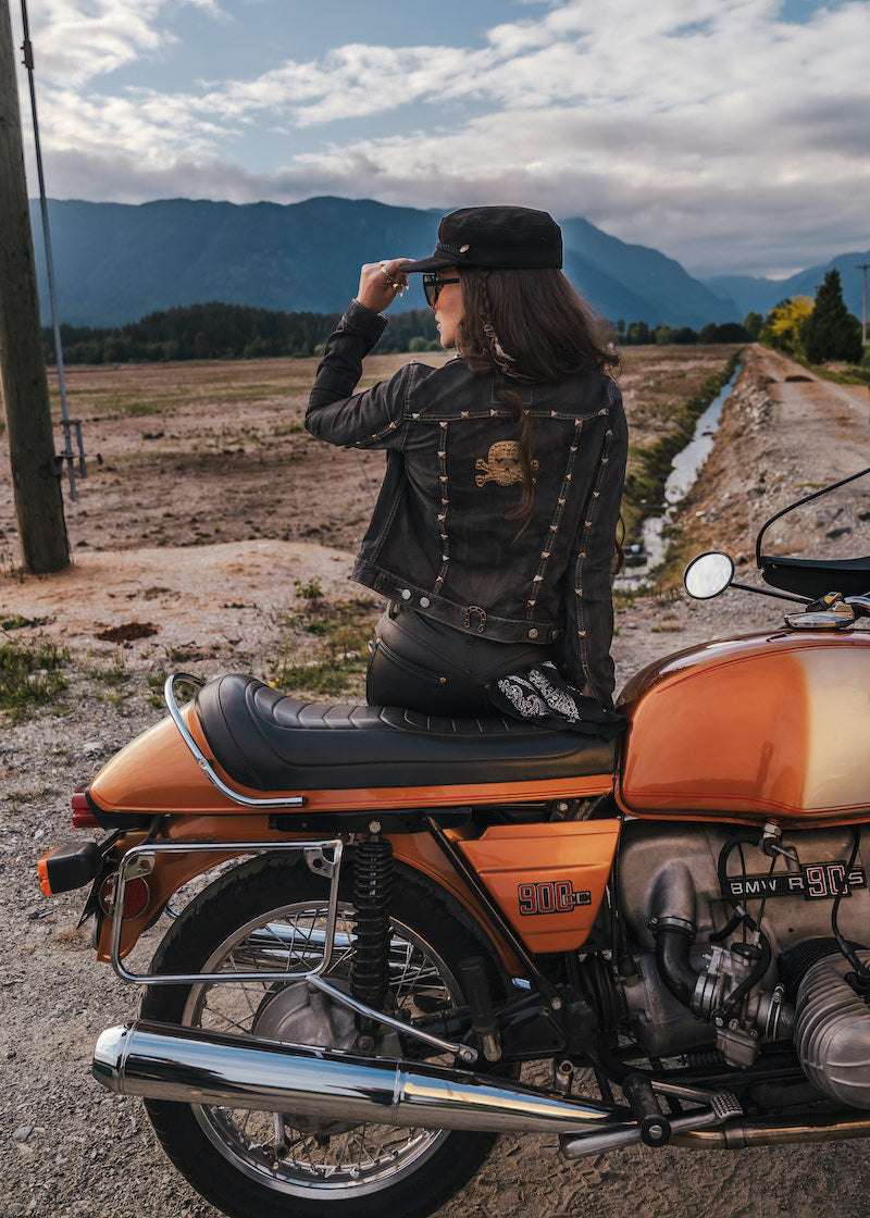 Person sitting on an orange motorcycle in a scenic outdoor setting with mountains in the background wearing Soul Sister since 1969