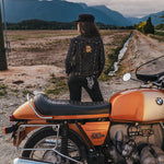 Person standing next to an orange motorcycle with mountains in the background wearing Soul Sister since 1969