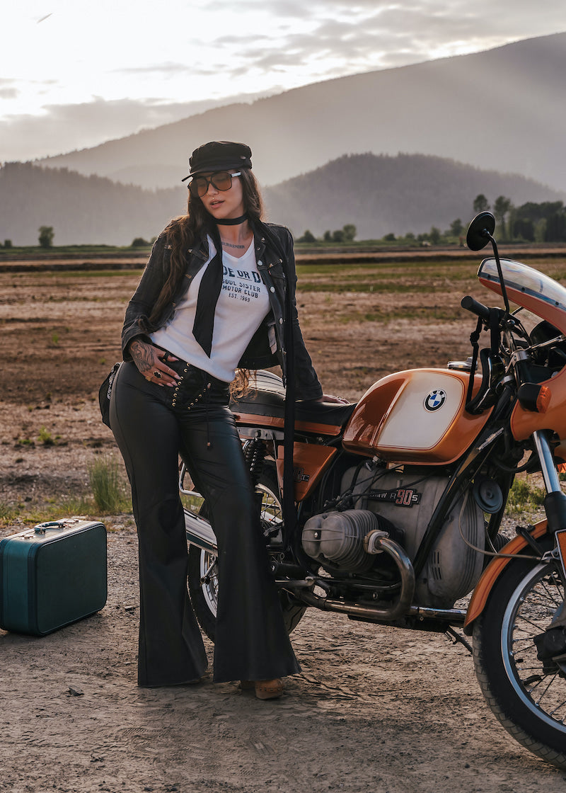 Woman standing next to a motorcycle in a desert landscape with mountains in the background wearing clothing designed and made by Soul Sister since 1969.