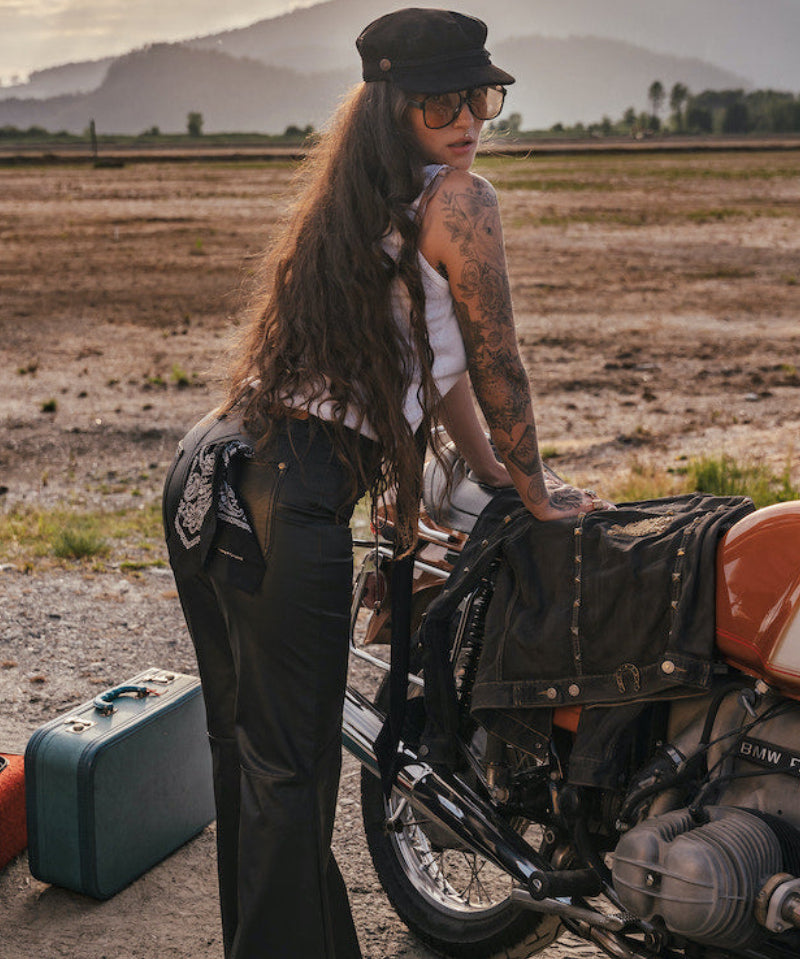 Person with tattoos standing next to a motorcycle in a desert landscape with mountains in the background wearing Soul Sister since 1969