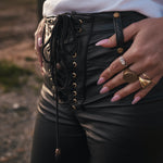 Person wearing a black lace-up vegan leather Bell bottom jeans with gold accents and a white top designed and made by Soul Sister since 1969.