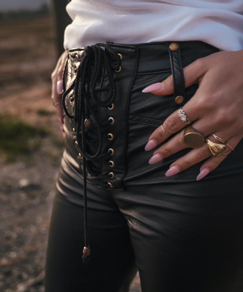 Person wearing a black lace-up vegan leather Bell bottom jeans with gold accents and a white top designed and made by Soul Sister since 1969.