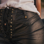 Close-up of black leather lace-up pants with gold buttons worn by a person designed and made by Soul Sister since 1969.