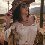Woman in an oversized hat and sunglasses with a tattoo on her neck, standing in a field wearing Soul Sister since 1969.