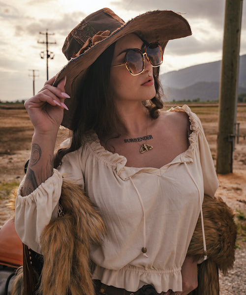Woman in an oversized hat and sunglasses with a tattoo on her neck, standing in a field wearing Soul Sister since 1969.