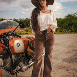 Woman in vintage attire standing next to a BMW motorcycle on a road with a scenic background wearing Soul Sister since 1969