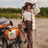 Person sitting on a BMW motorcycle wearing a white blouse, brown pants, and a hat with a fur-lined coat wearing Soul Sister since 1969.
