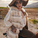Person wearing a fur vest and wide-brimmed hat sitting on a motorcycle in an open field. Wearing Soul Sister since 1969