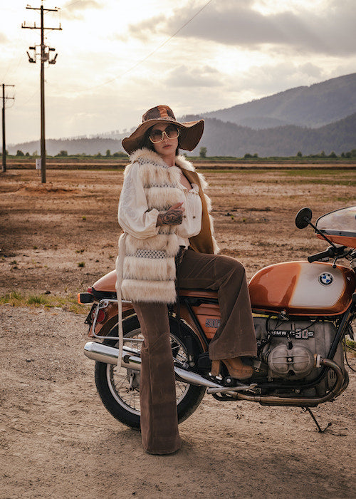 Person sitting on a motorcycle in a desert-like setting with mountains in the background wearing Soul Sister since 1969