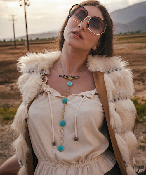 Woman wearing sunglasses and a fur vest in a desert landscape wearing soul sister since 1969