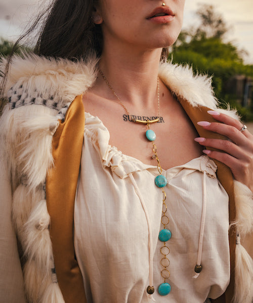 Person wearing a white blouse with turquoise beads and gold necklace, outdoors. wearing soul sister since 1969